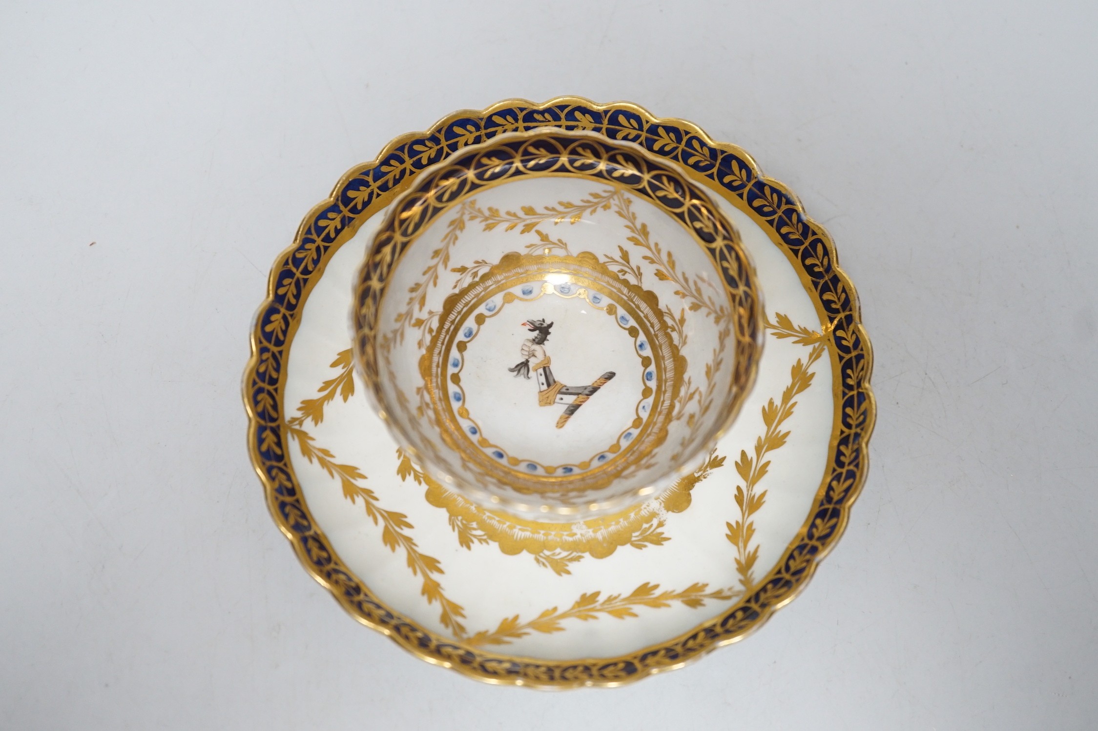 An 18th century Caughley rare teabowl and saucer painted with a crest of an arm clutching a dragon encircled by three gilt borders, 6cm tall overall